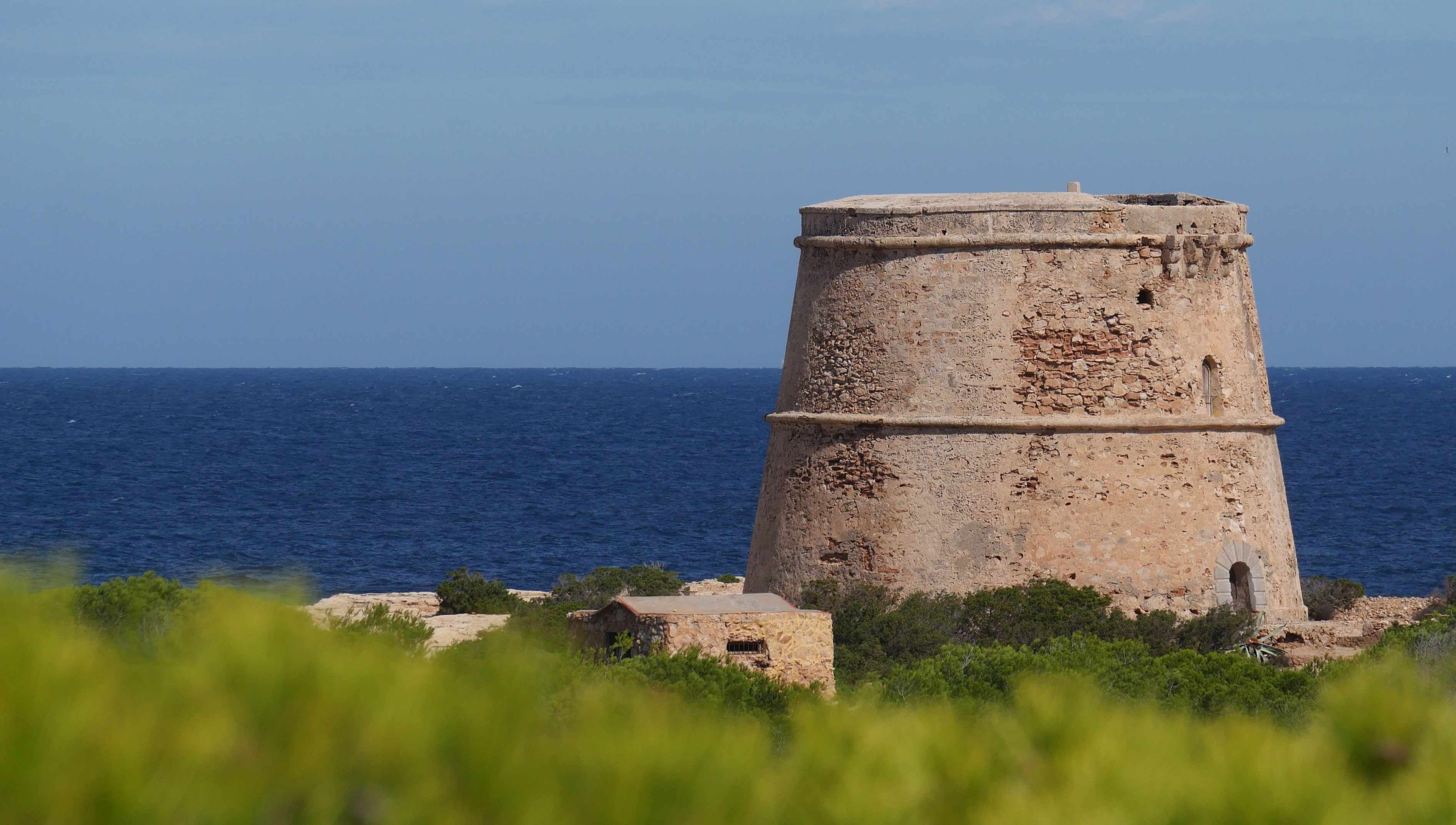 An old stone watchtower above the pines by the sea in Ibiza